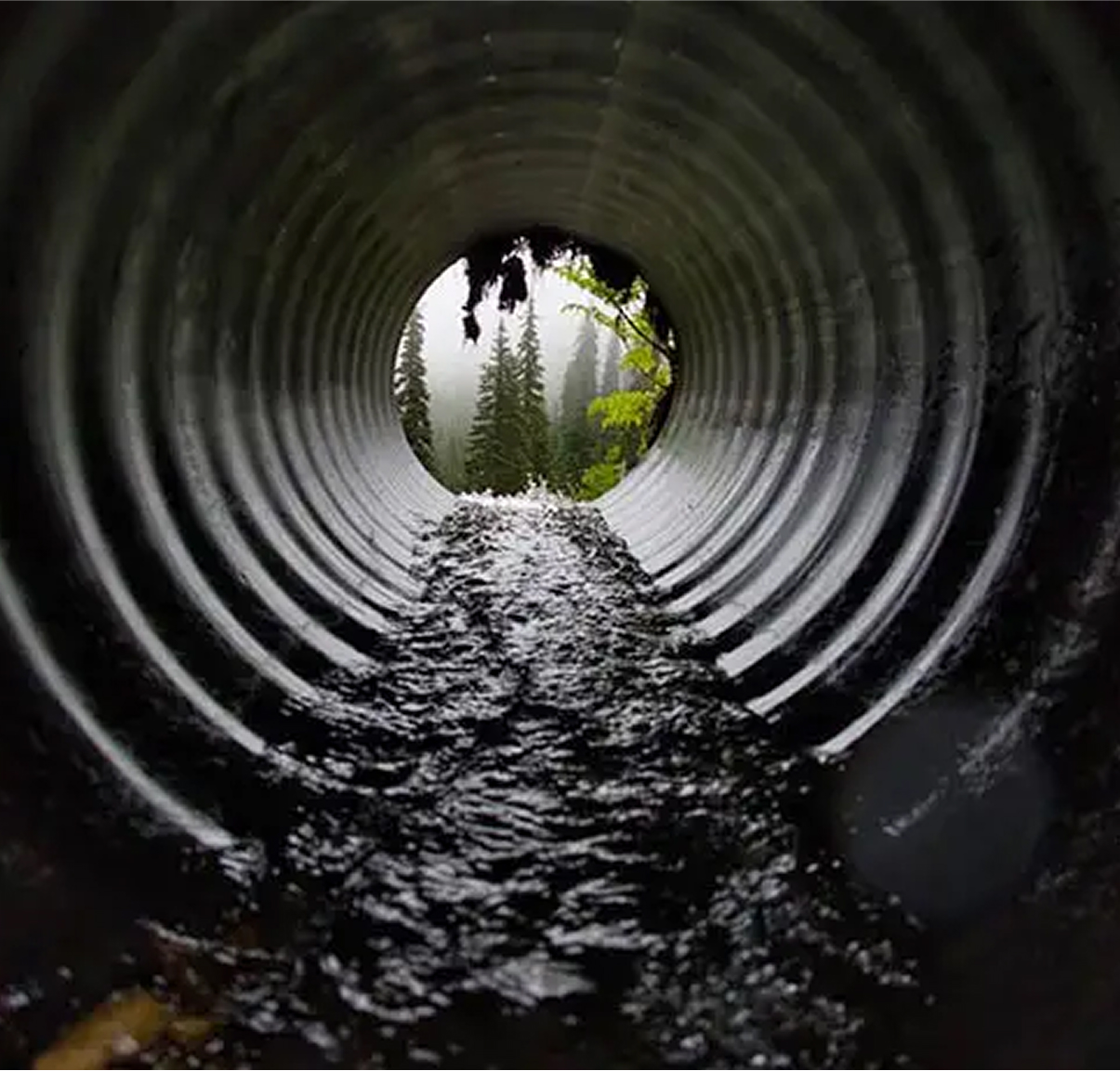 View inside a large drainage pipe with water flowing through.