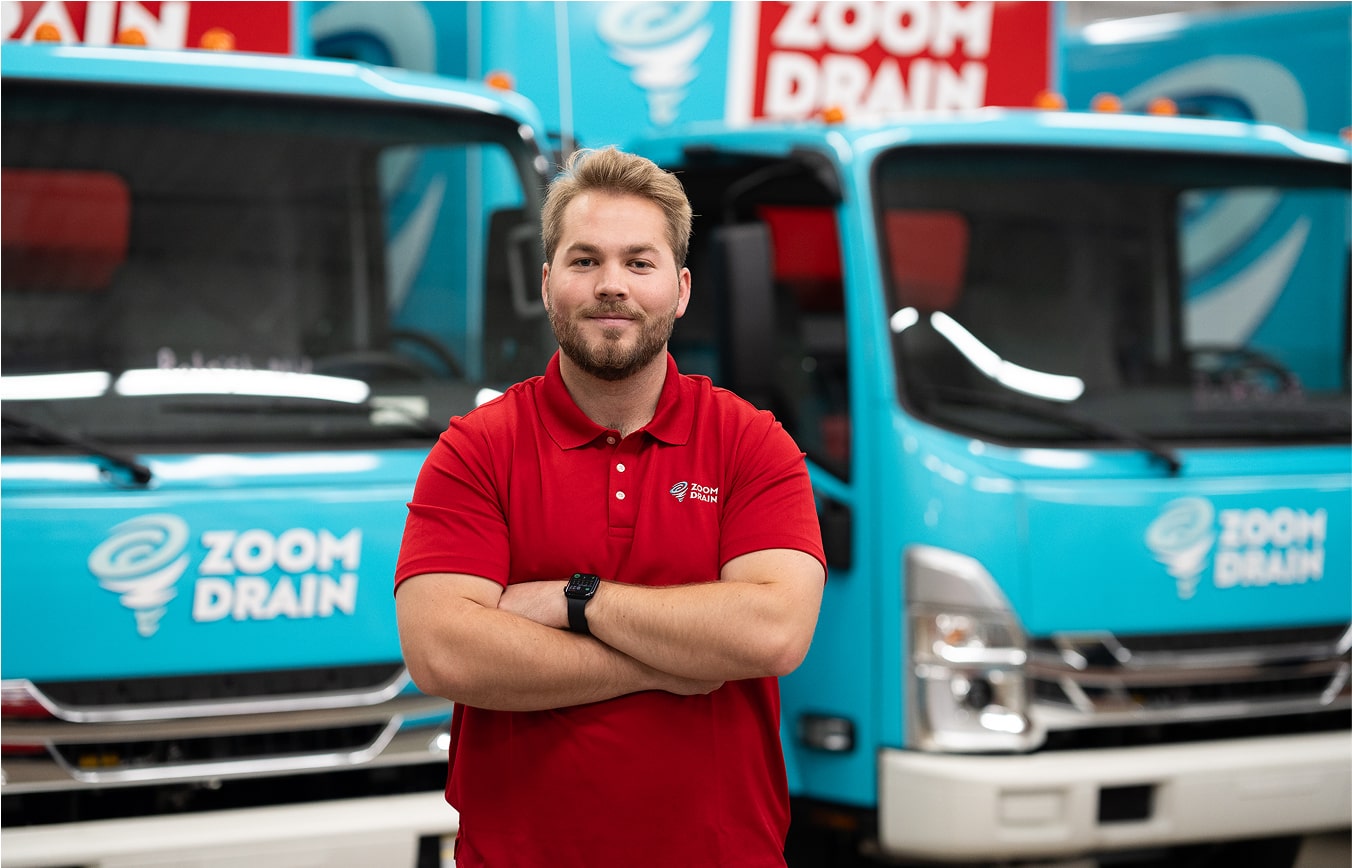 Zoom Drain employee standing with arms crossed in front of company trucks.