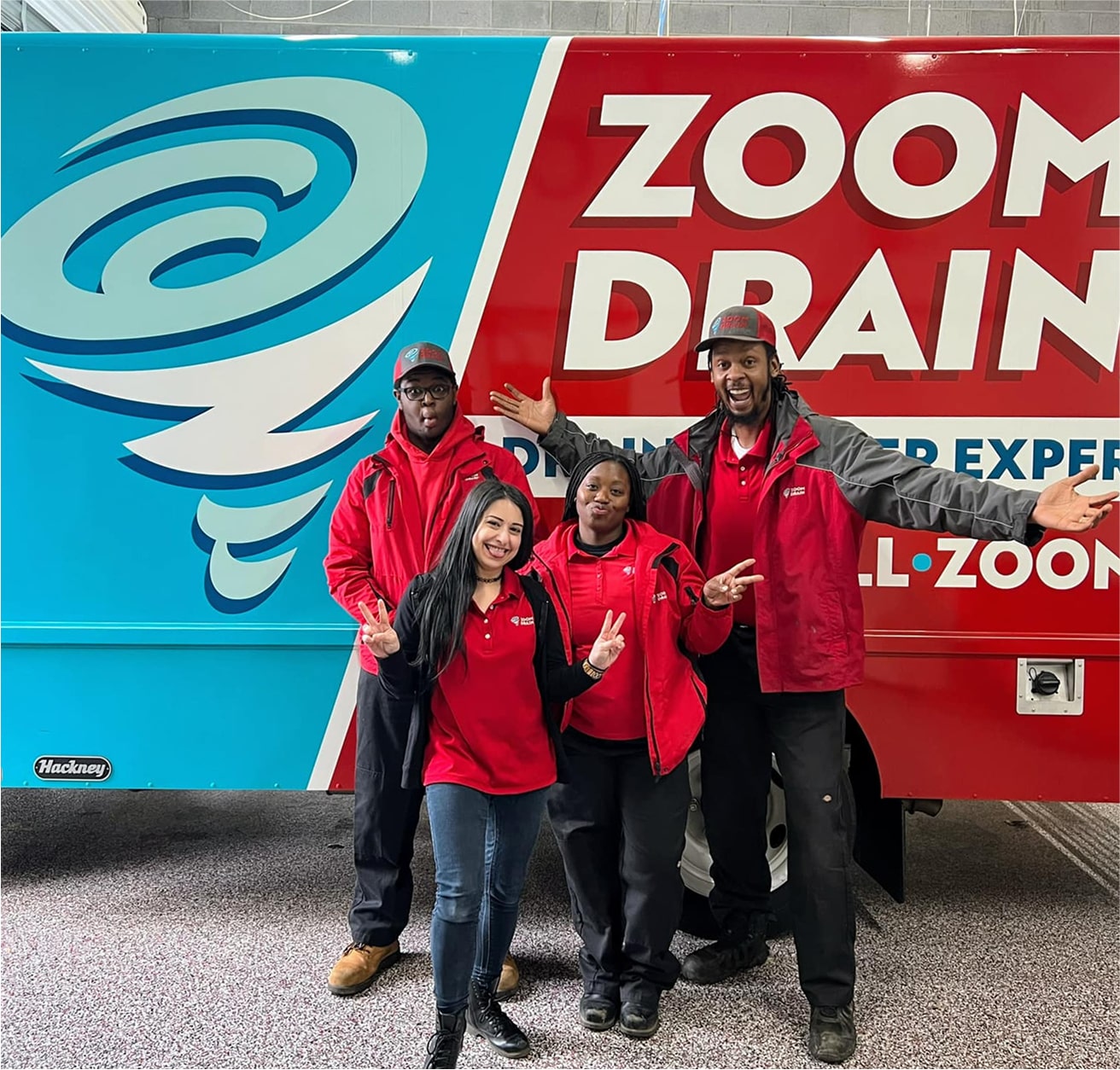 Group of Zoom Drain employees standing together in front of branded vans.
