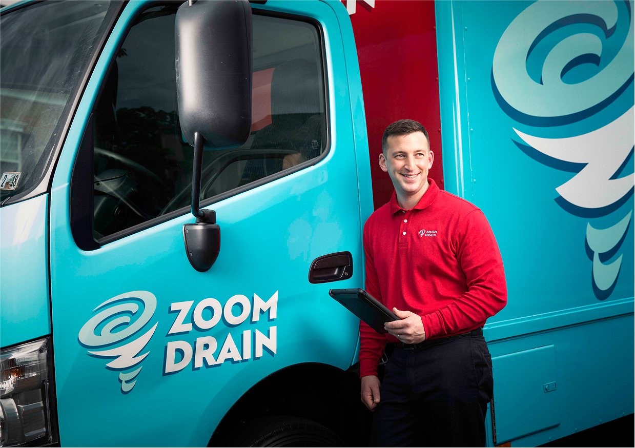 Technician in red shirt standing next to a Zoom Drain service van.