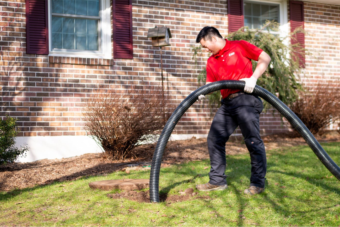 Worker inserting a large hose into the ground for sewer repair.