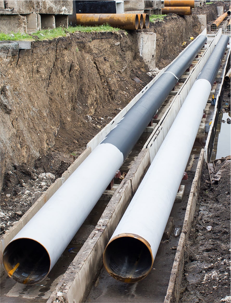 Large sewer pipes stacked in a dirt trench ready for installation.
