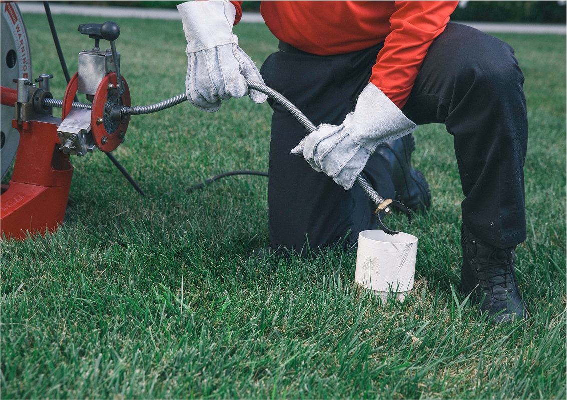 Technician digging in grass to locate and clear a drain blockage.