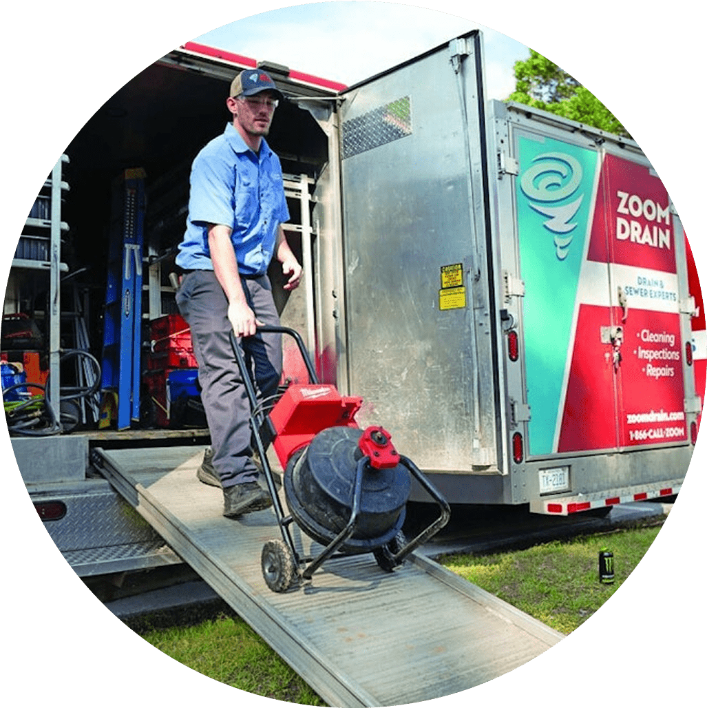 Workers operating drain cleaning equipment outside a building.