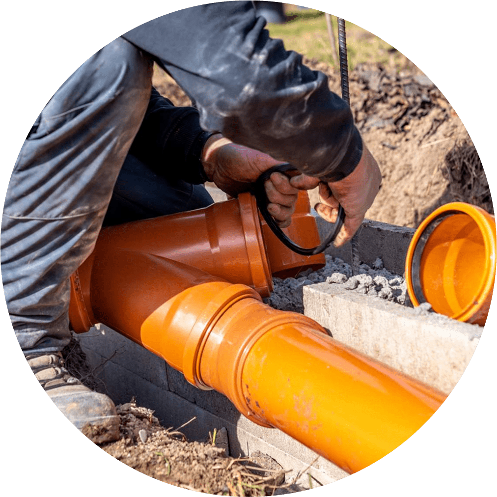 Worker installing a large orange drainage pipe outdoors.