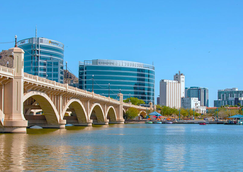 View of Tempe Town Lake with bridge and city buildings in the background.