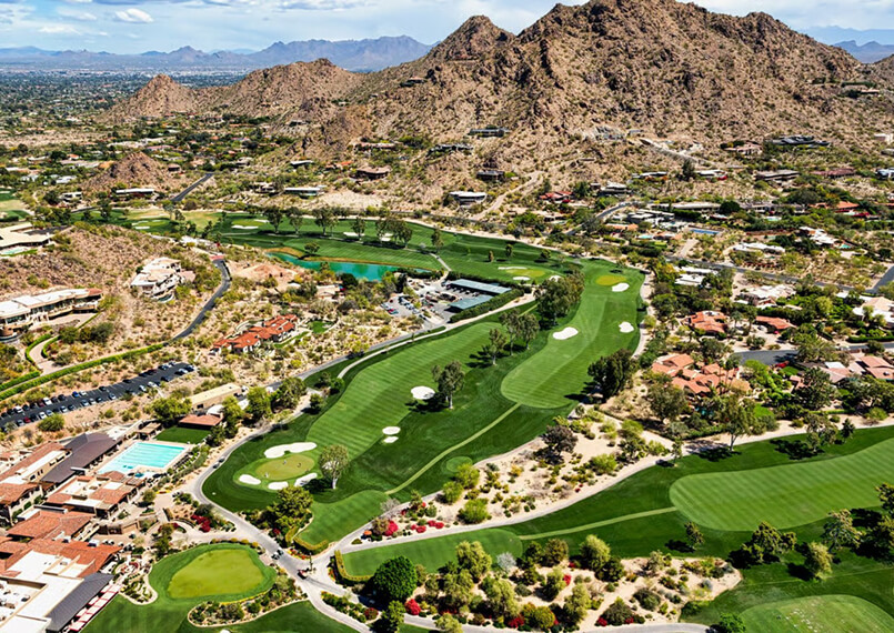 Aerial view of a golf course surrounded by desert mountains and houses.