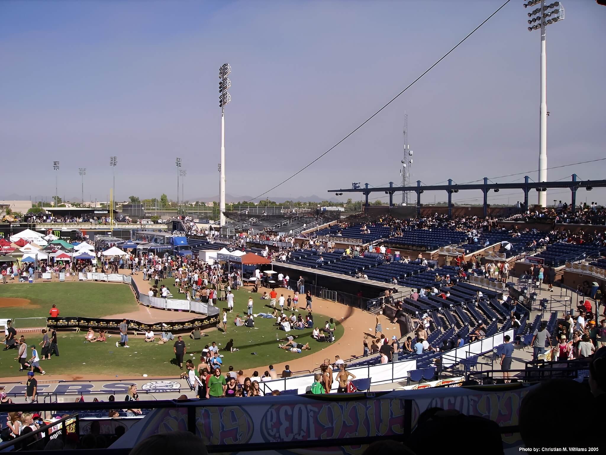 Crowd gathering at Peoria Sports Complex in Peoria, Arizona, with spectators in the stands and people on the field during a daytime event under clear skies.