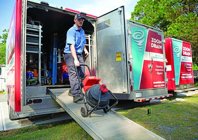 Workers operating drain cleaning equipment outside a building.