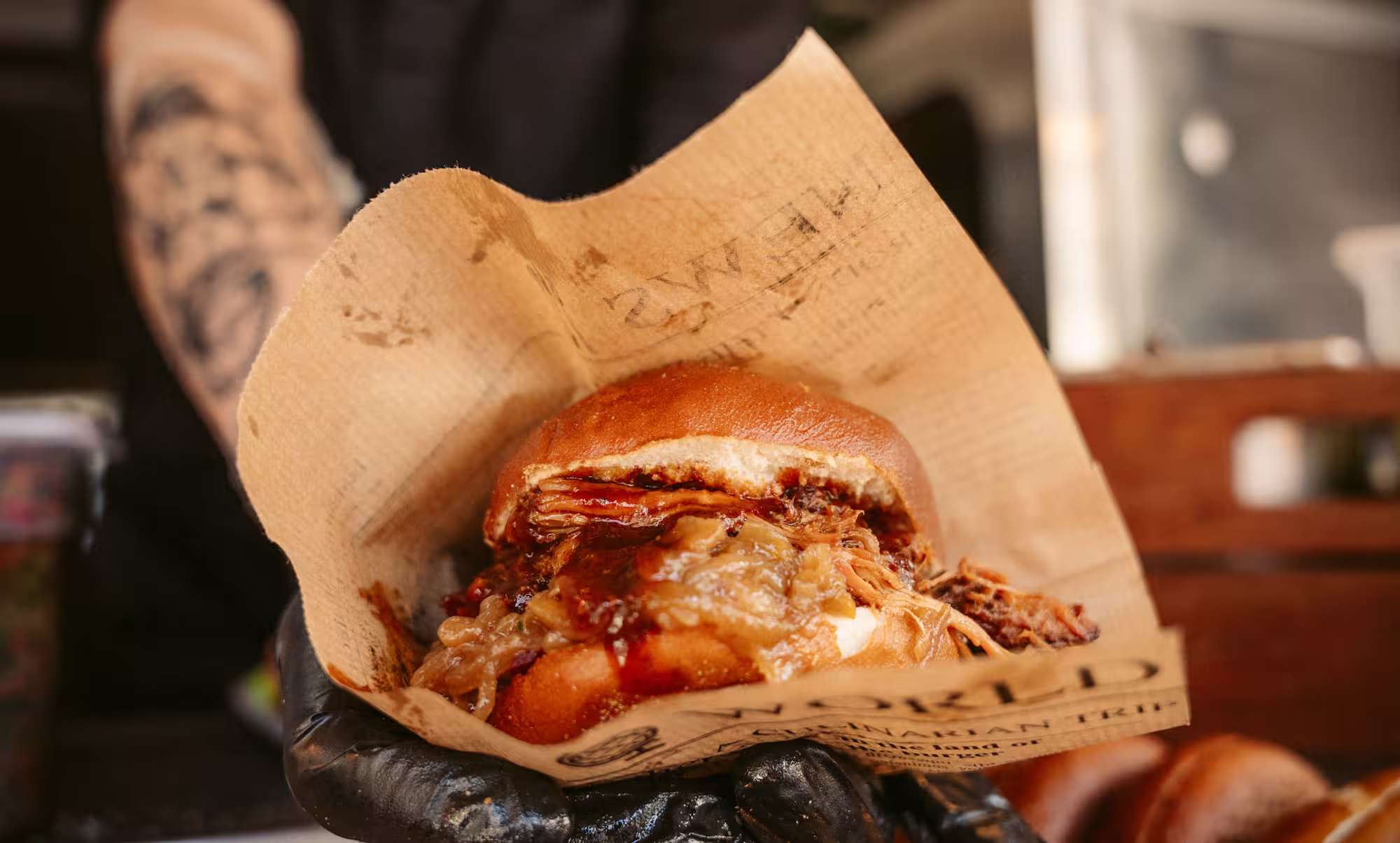 Saftiger Pulled Pork Burger mit karamellisierten Zwiebeln in einer handgehaltenen Papiereinlage.