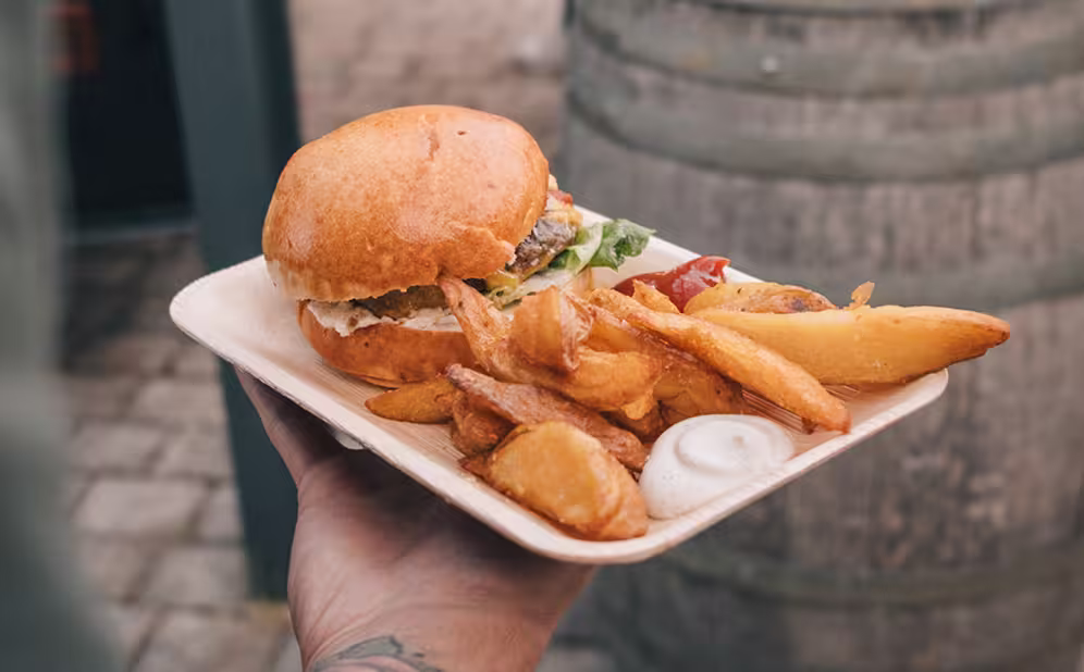 Hand, die einen Teller mit einem Burger, dicken Pommes und Saucen hält.
