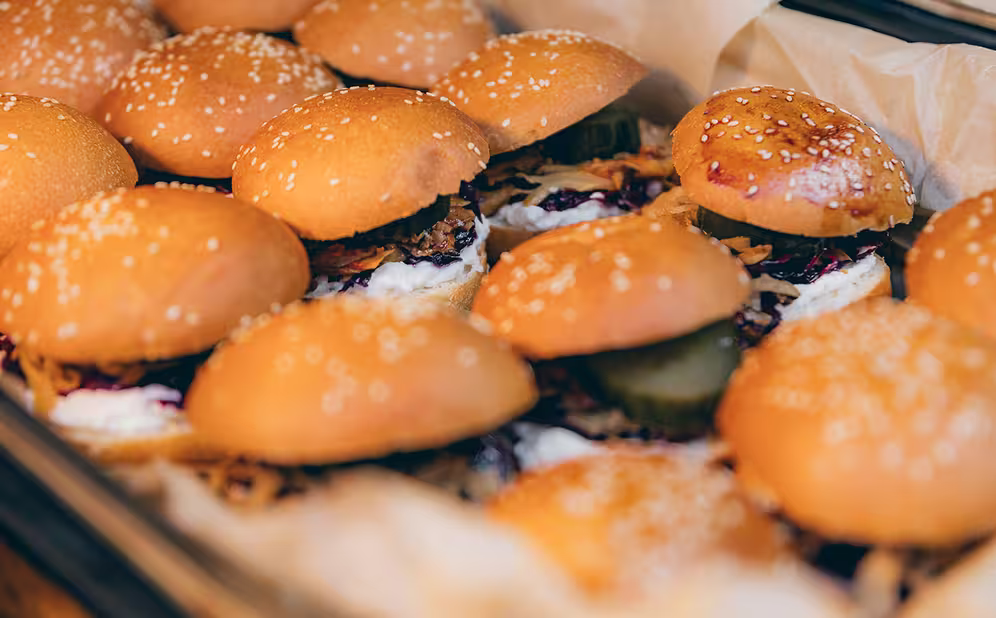Nahaufnahme von mehreren Burger-Sandwiches mit Sesambrötchen, gefüllt mit saurer Sahne, Gurkenscheiben und anderen Belägen in einer Kiste.