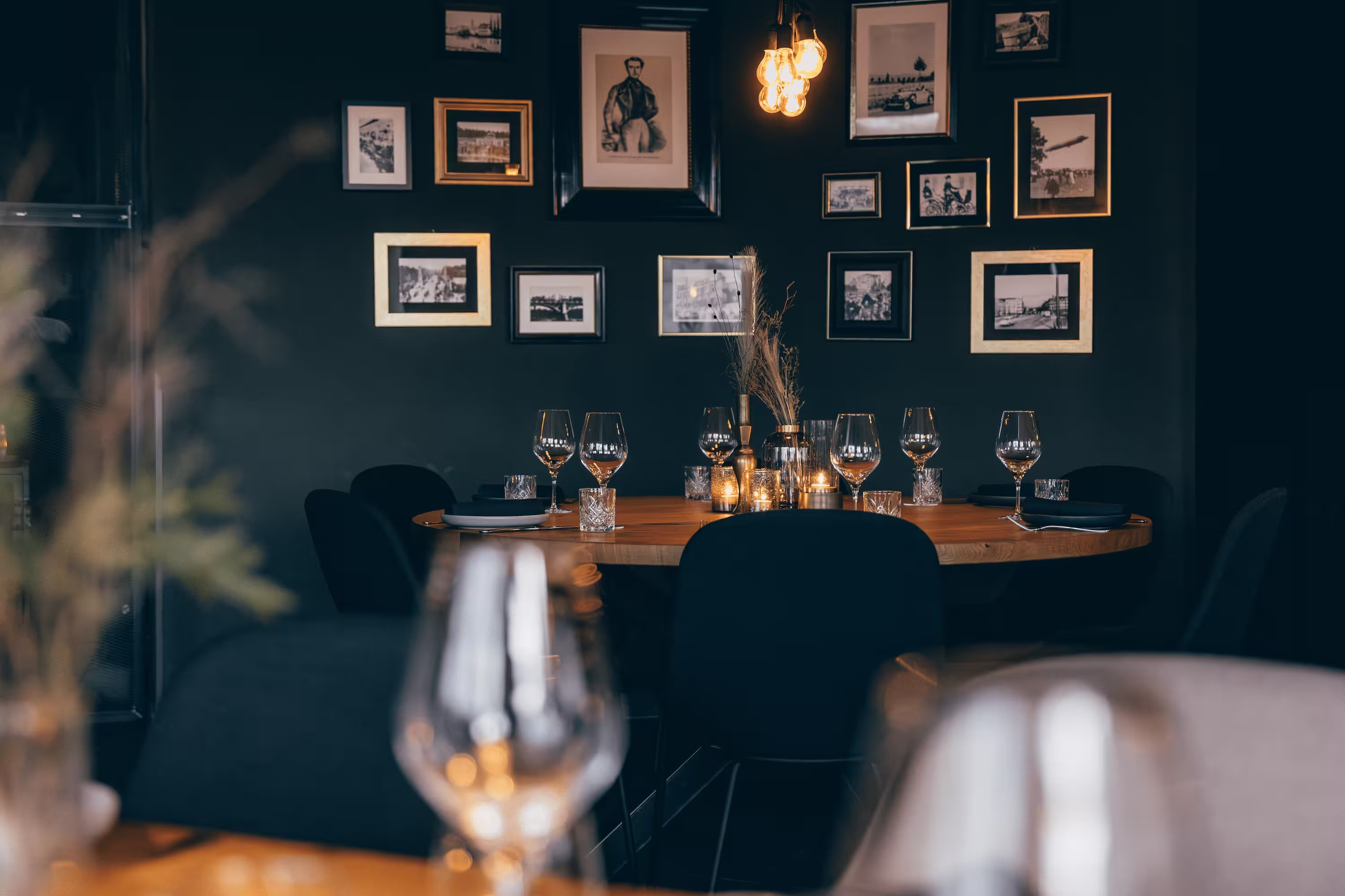 Gemütlicher Tisch in der Cantine Royale mit Weingläsern, Kerzen und gerahmten Bildern an der Wand.