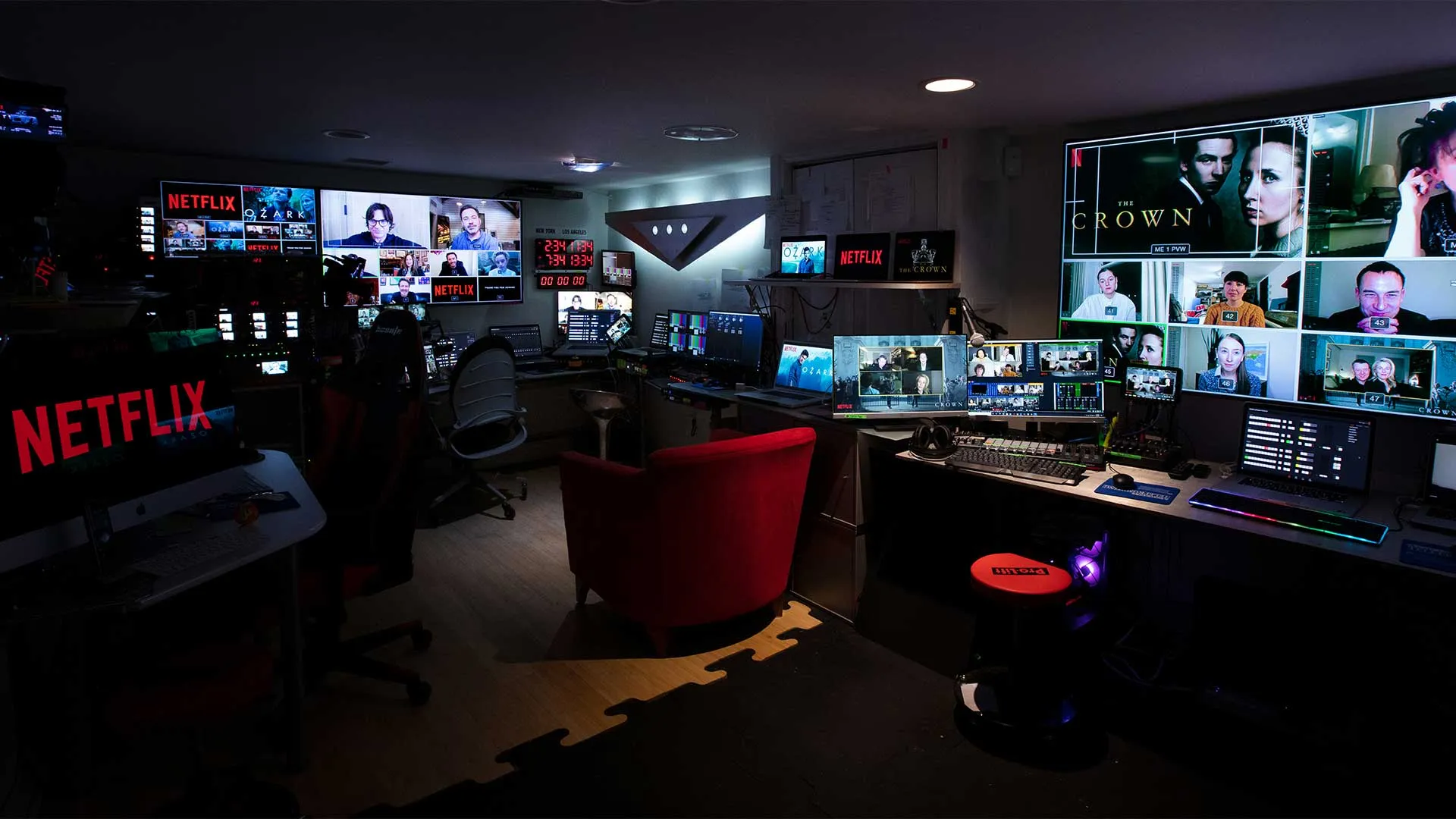 Dark control room with multiple monitors displaying Netflix shows and virtual meeting participants, including screens for Ozark and The Crown.