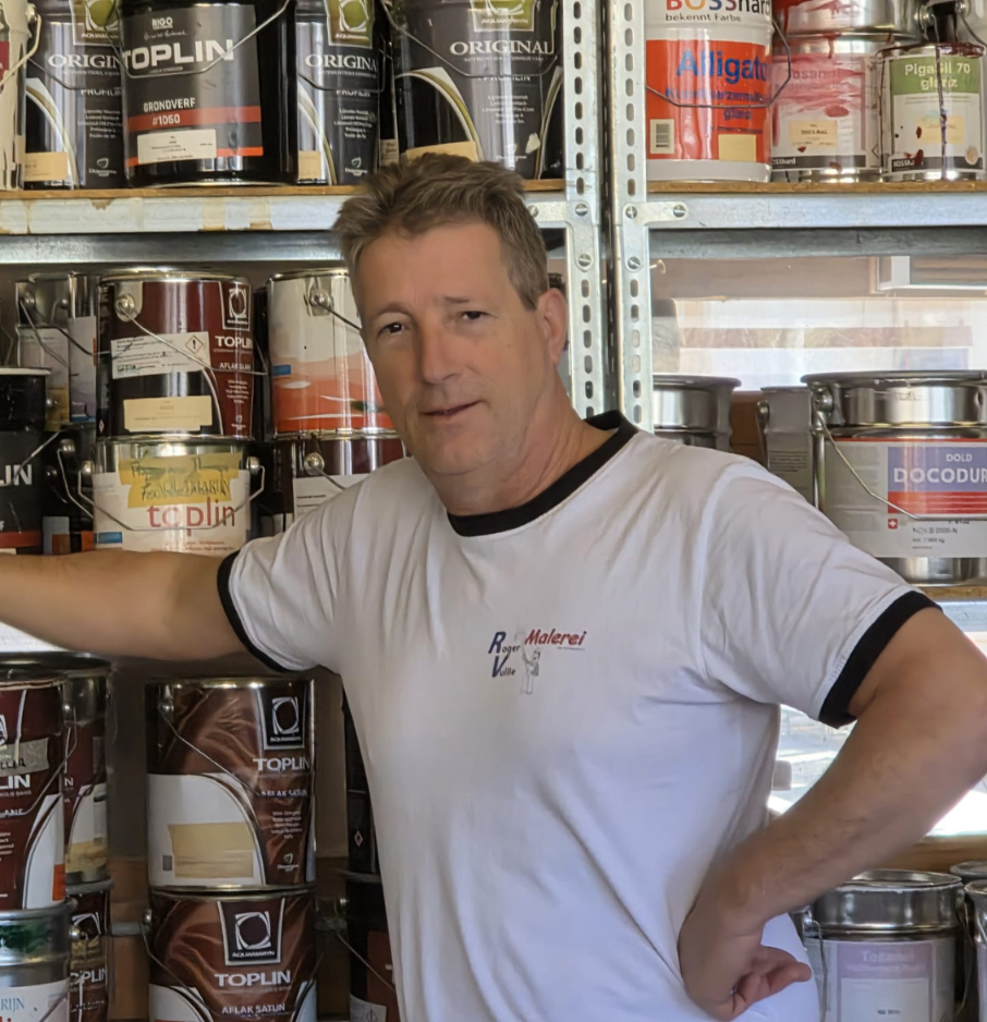 Portrait von Roger Vuille. Hinter ihm ein Regal mit Farbkesseln.