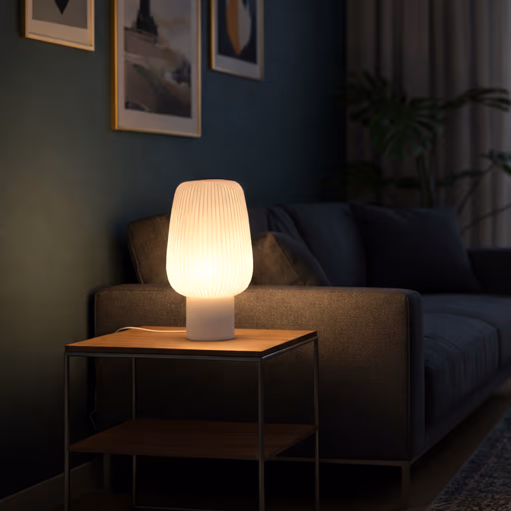Glowing modern table lamp on a wooden side table next to a dark gray sofa in a dimly lit living room.