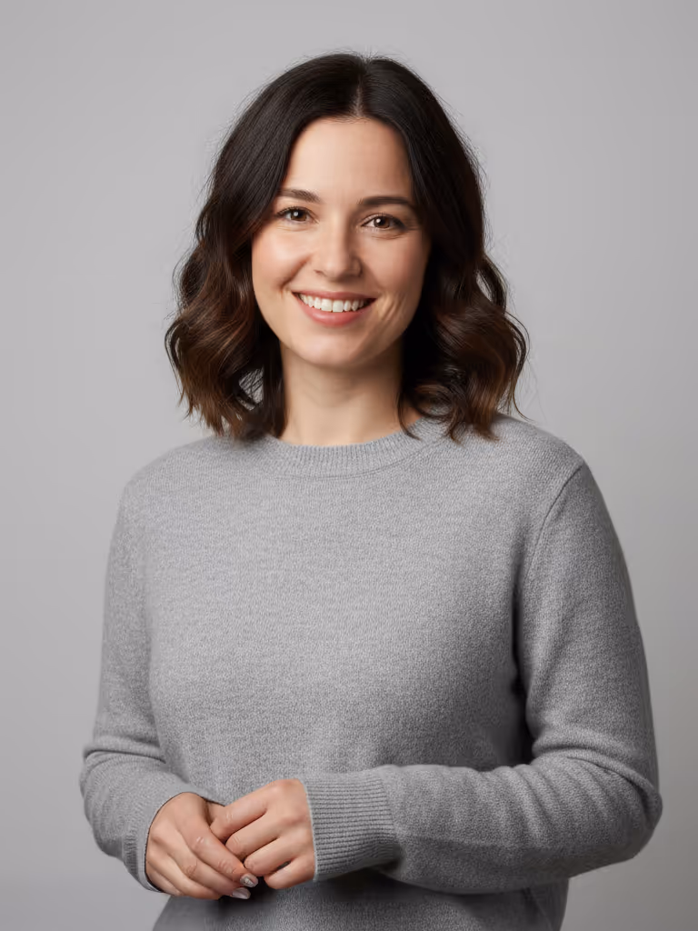 Smiling woman with shoulder-length wavy dark hair wearing a gray sweater against a plain gray background.