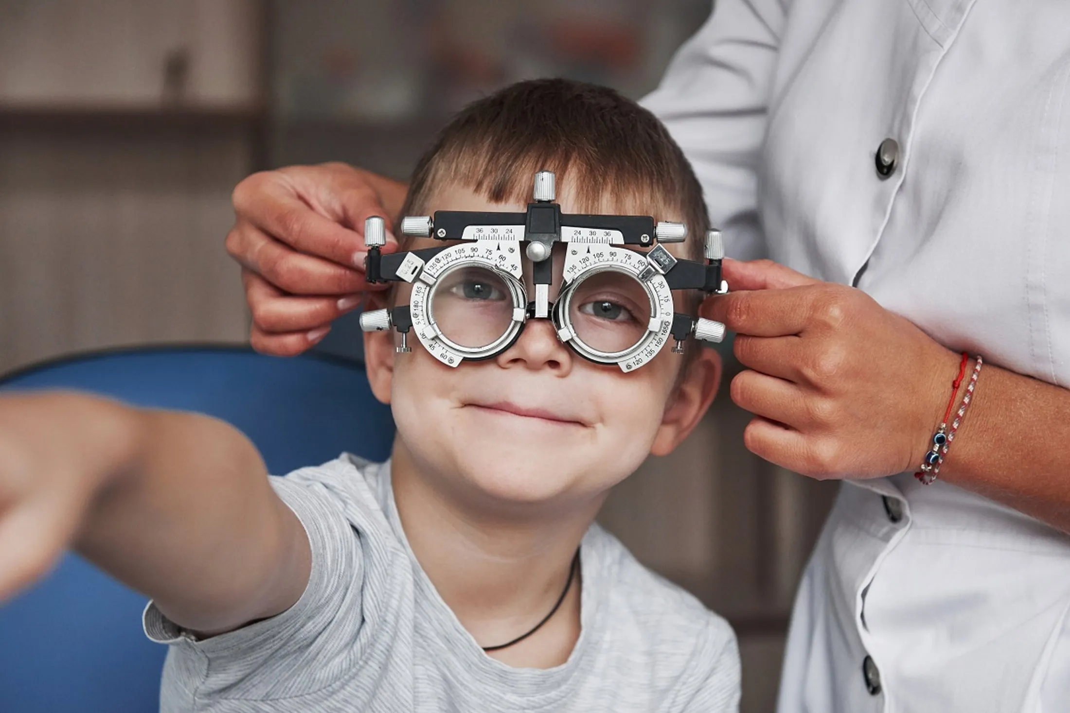 Child smiling and raising hand while an optometrist adjusts eye exam glasses on their face.