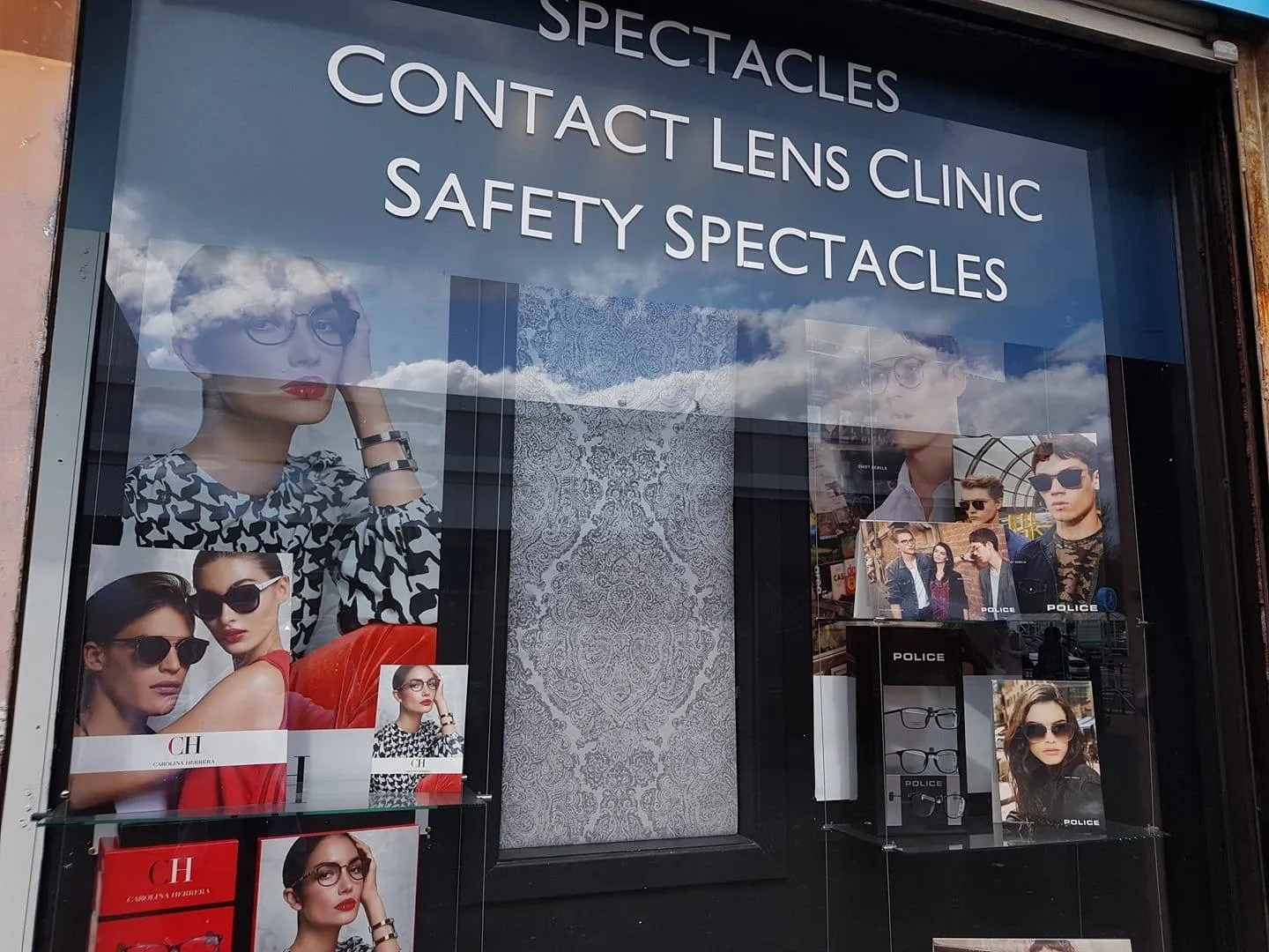 Shop window displaying eyewear ads and products under words Spectacles Contact Lens Clinic Safety Spectacles.