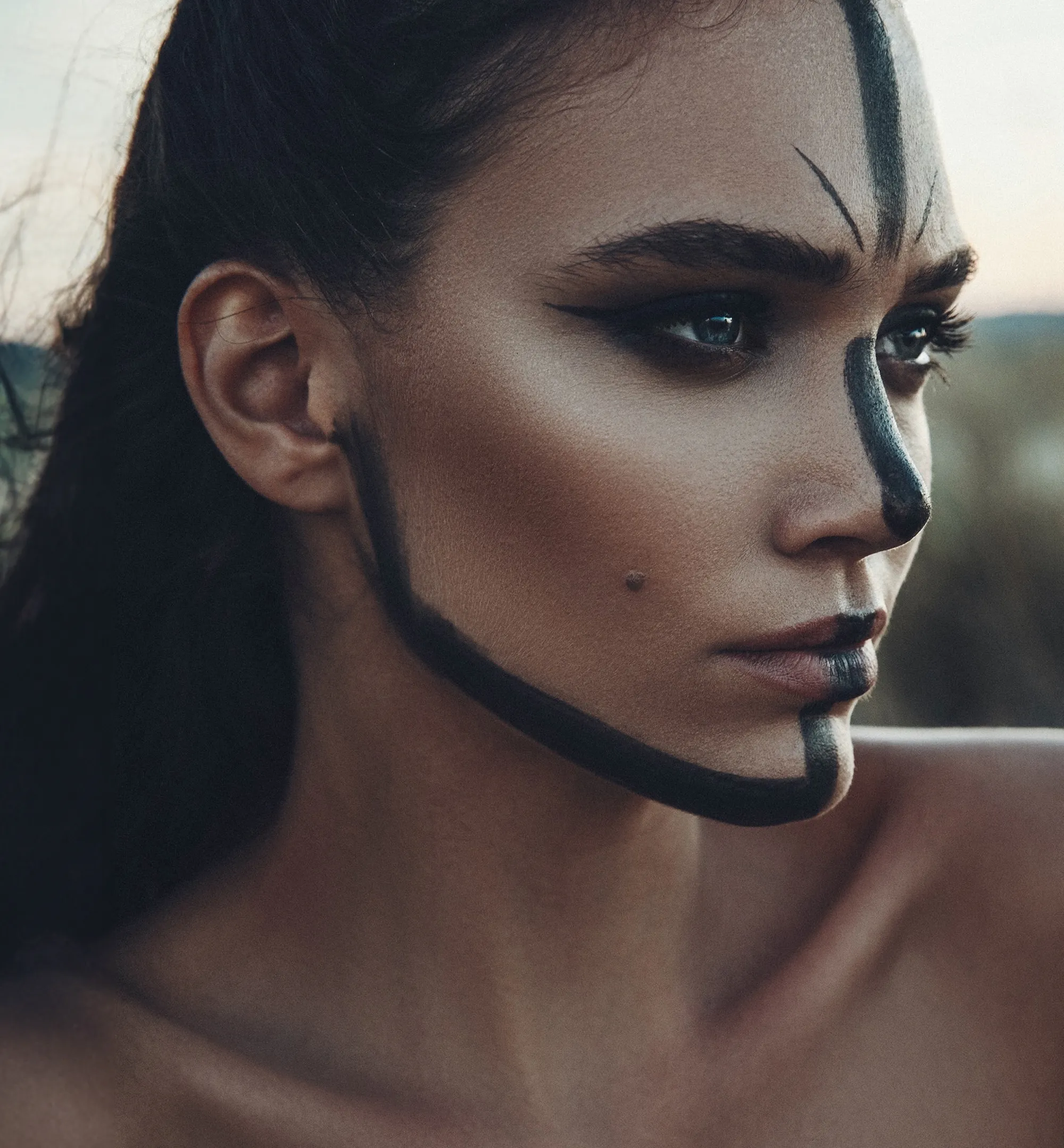 Frau mit dunkler Gesichtsbemalung in Form von Linien auf der Stirn, an der Nase, am Kinn und entlang des Kiefers.