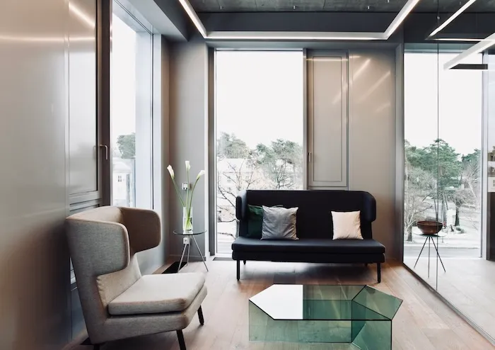 Moderne Lounge im Wartebereich mit Sesseln, schwarzem Sofa, Glastisch und großen Fenstern mit Blick nach draußen.
