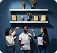 Three people in white shirts pointing at trophies and awards on blue wall shelves.