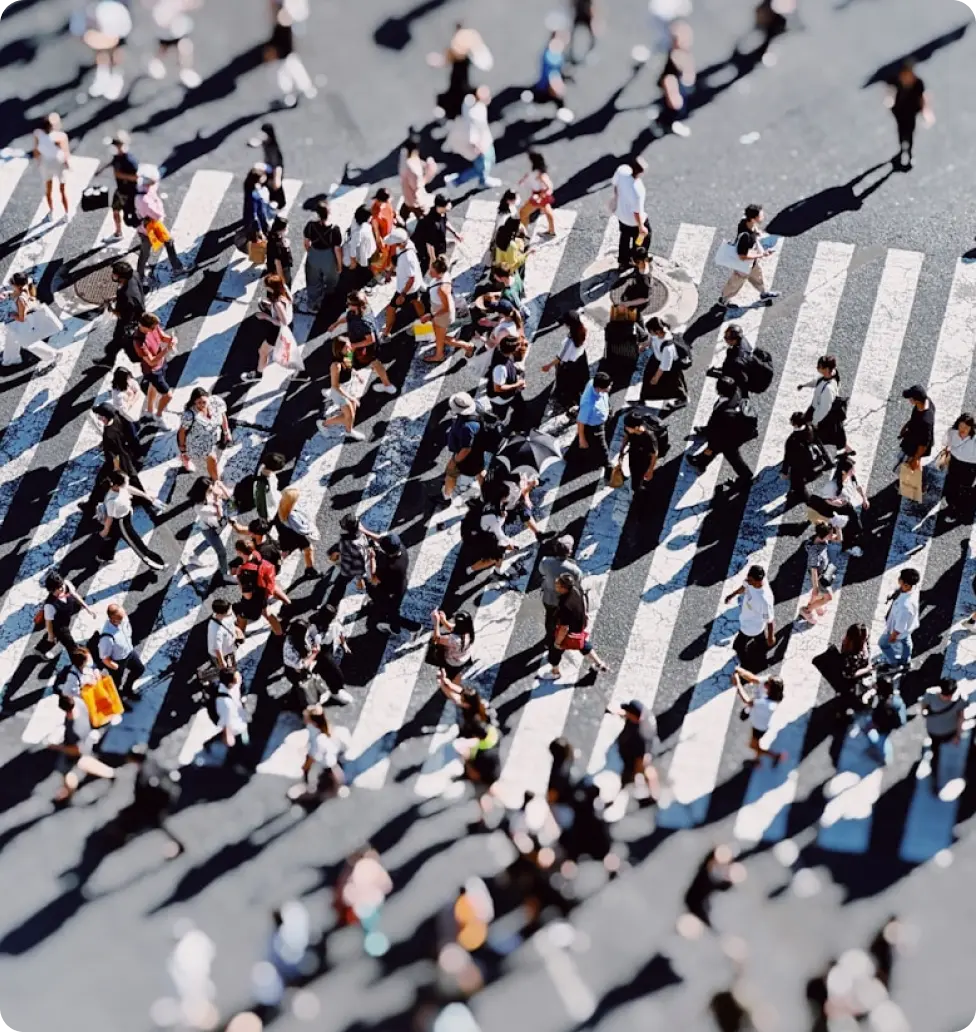 Overhead view of diverse pedestrians crossing a busy street with long shadows on a sunny day.