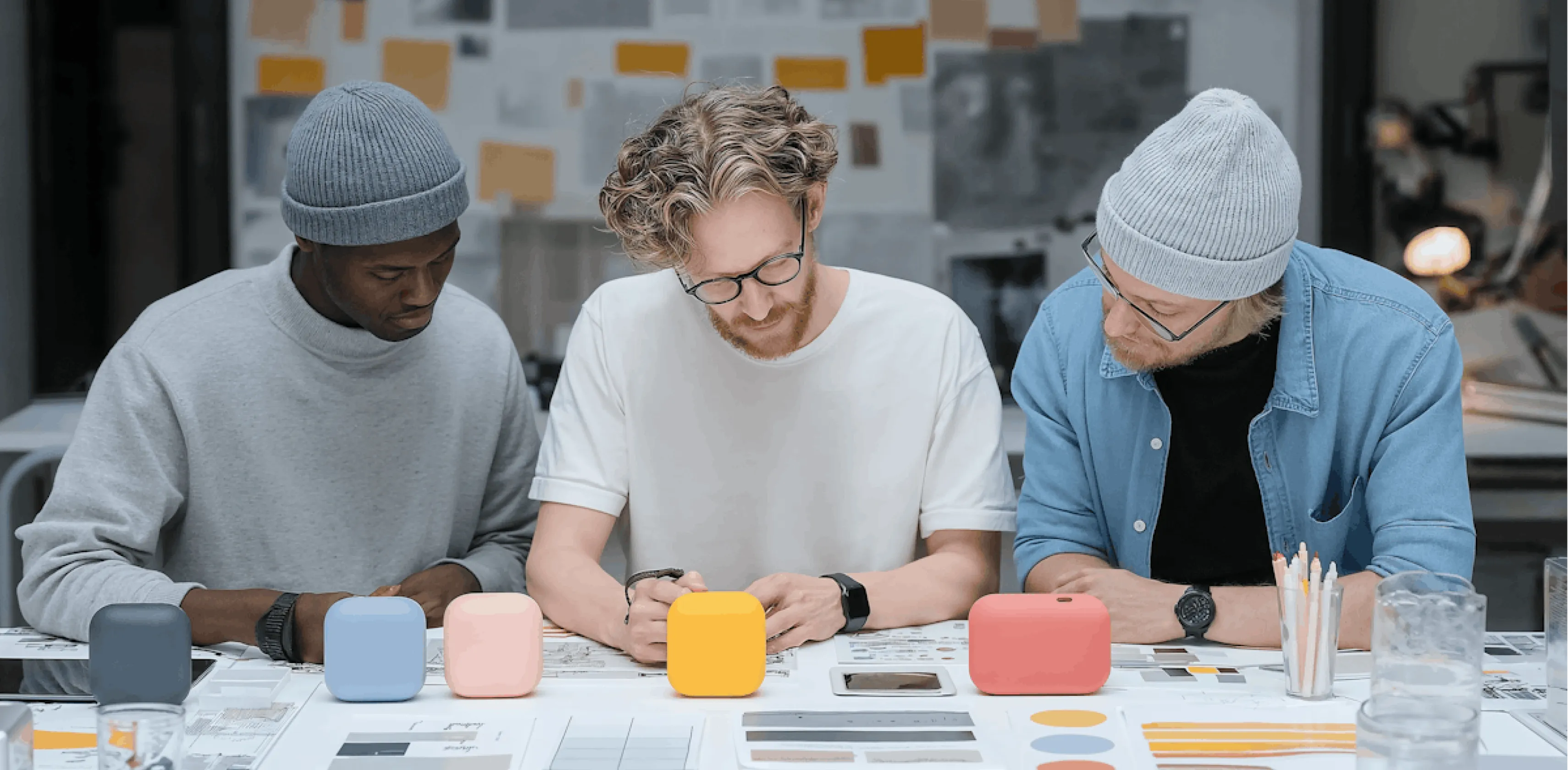 Three men sitting at a table reviewing documents with colorful cube models and design materials laid out.