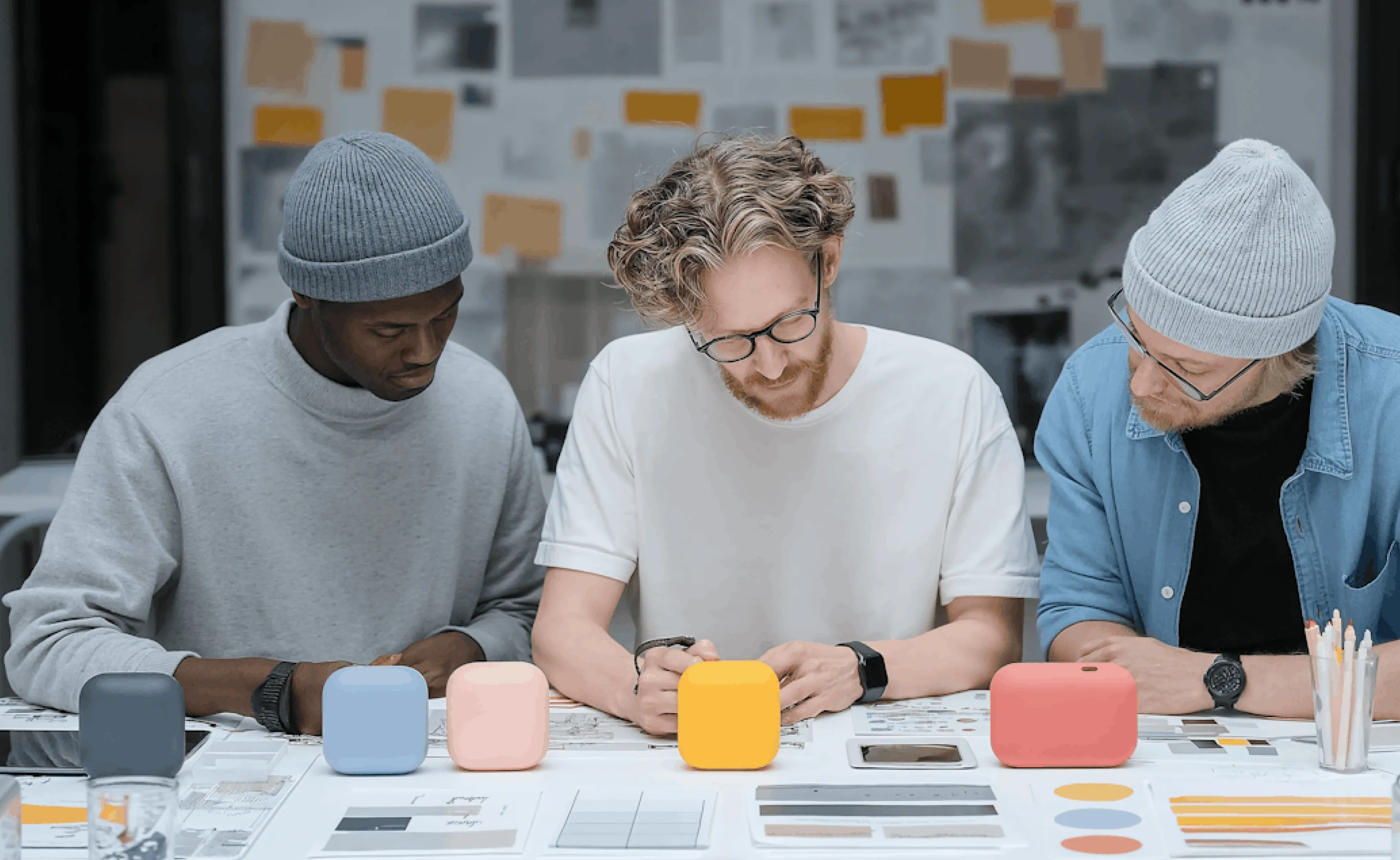 Three men collaborating over color swatches and sketches at a table in a creative workspace.