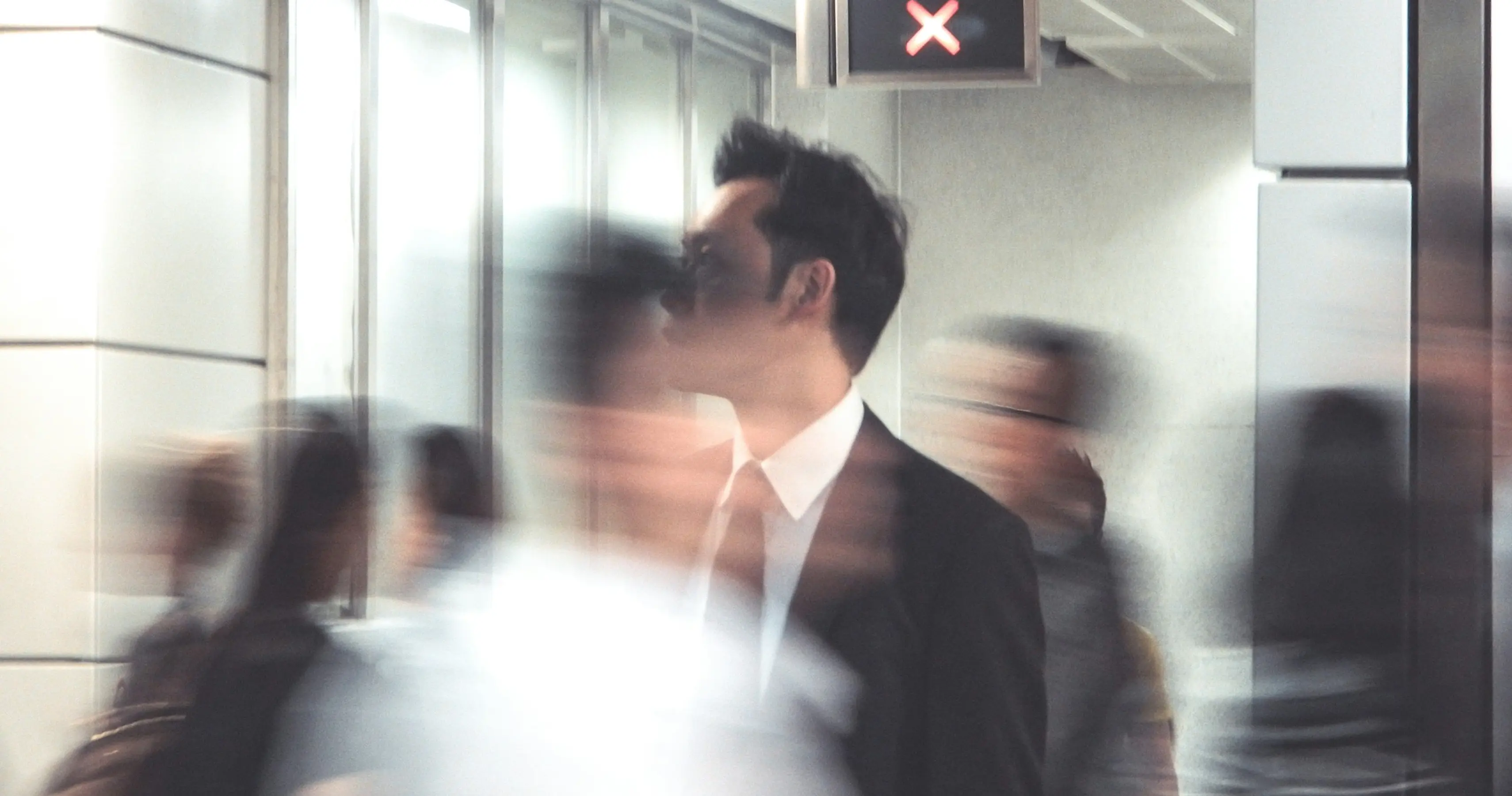 Man in a suit standing still among blurred people walking in an indoor urban setting.