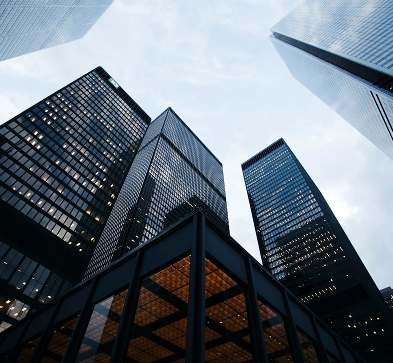 Low-angle view of tall glass office buildings against a cloudy sky at dusk.