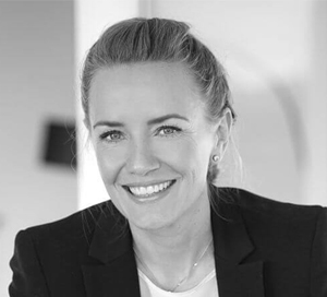 Smiling woman with light hair pulled back, wearing a dark blazer and earrings.