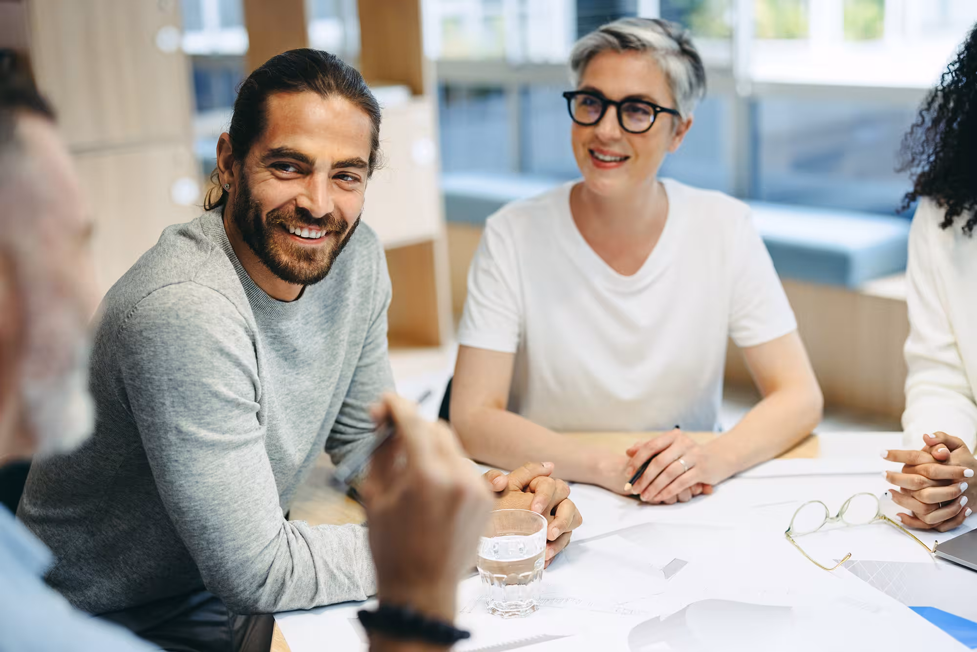 Three people sitting at a table engaged in a friendly discussion, with documents and a glass of water on the table.