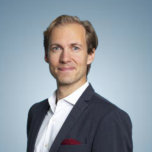 Smiling man with light brown hair wearing a dark blazer, white shirt, and red pocket square against a blue gradient background.