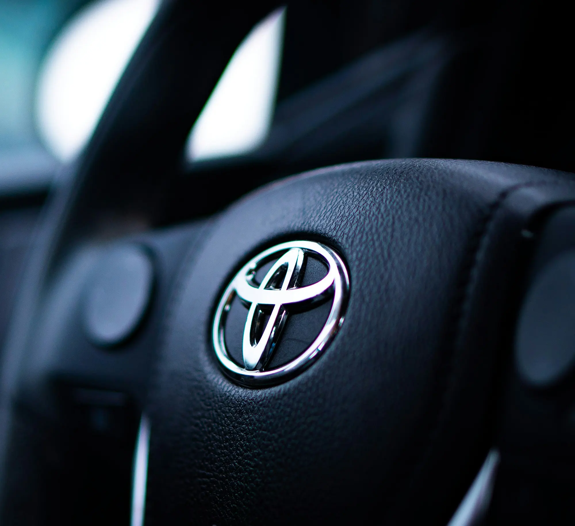 Close-up of a Toyota car steering wheel emblem on black leather.