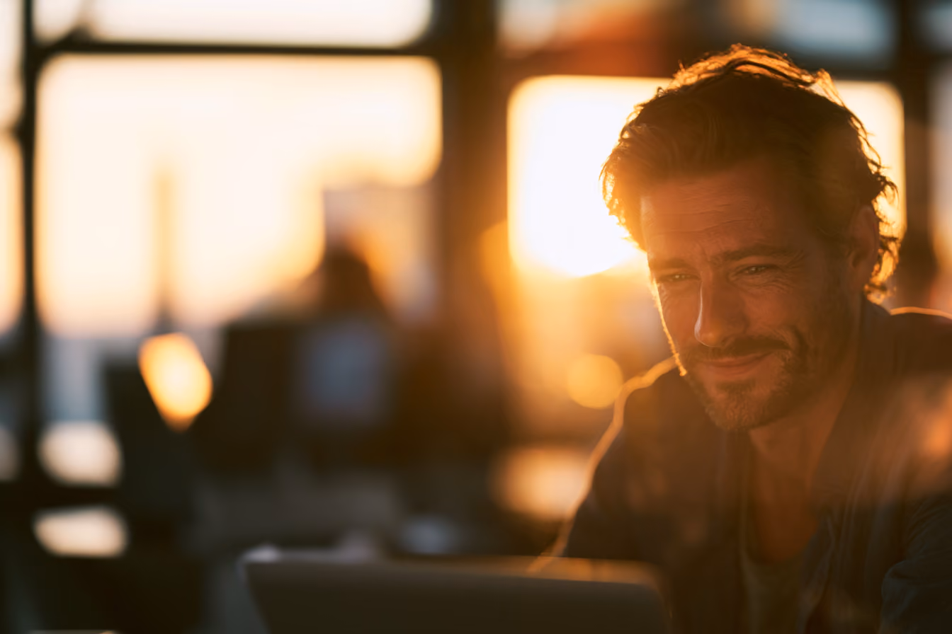 Man working at a computer in warm evening light.