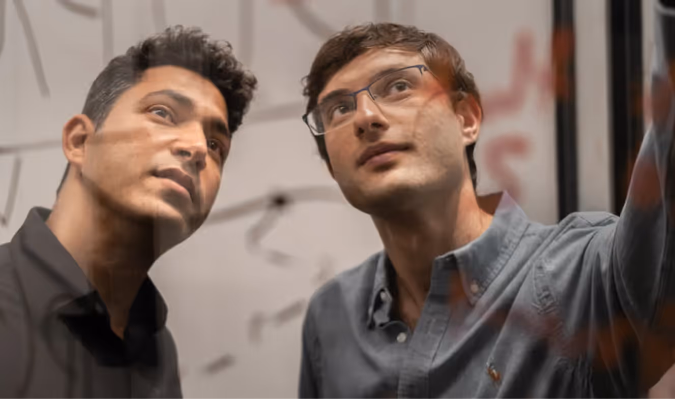 Two men looking intently at writing or drawings on a transparent board in a work or brainstorming session.