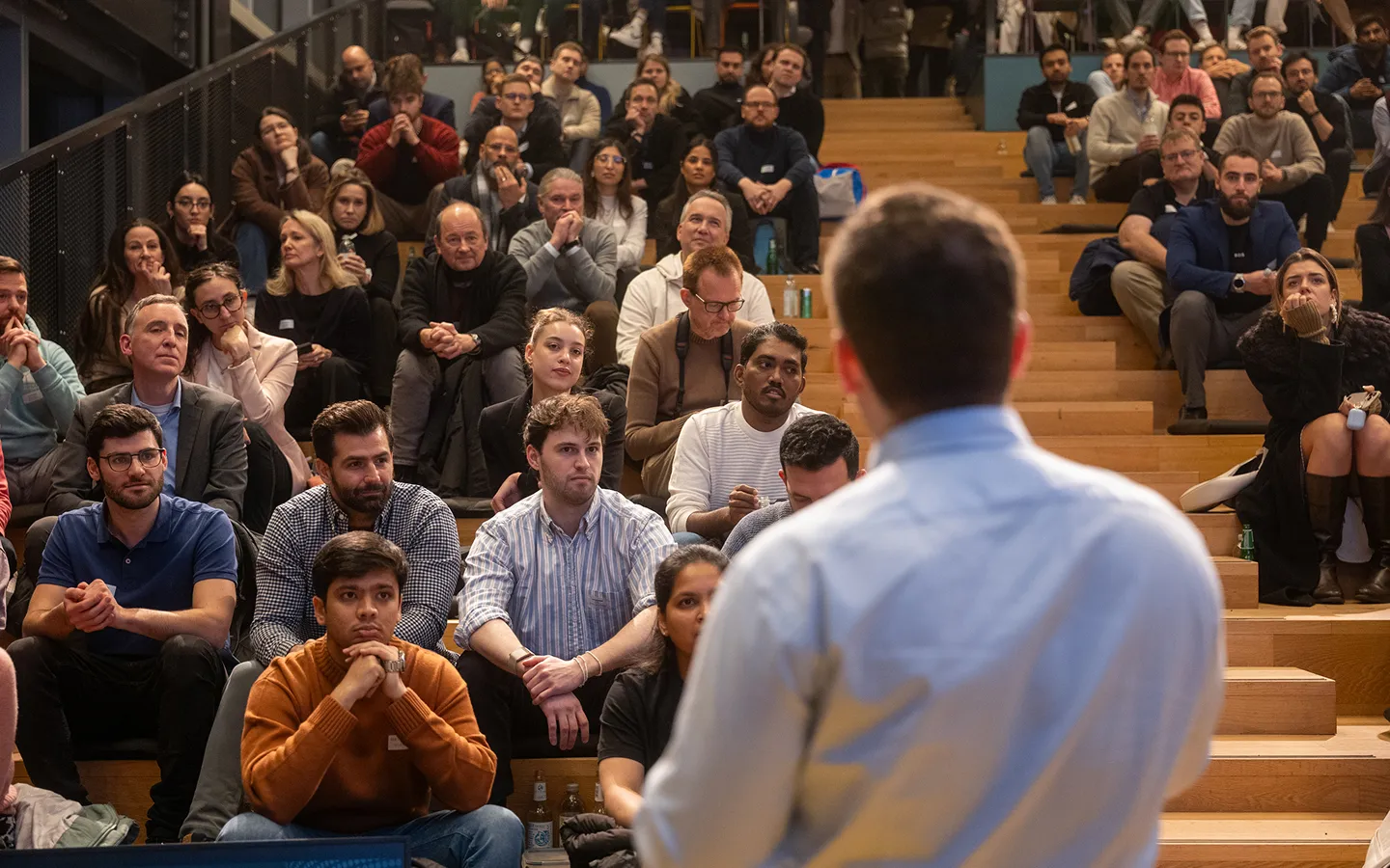 Audience attentively listening to a speaker in a tiered seating auditorium.