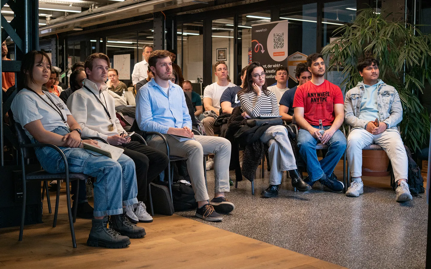 A diverse group of young adults attentively seated indoors, listening to a presentation or lecture.