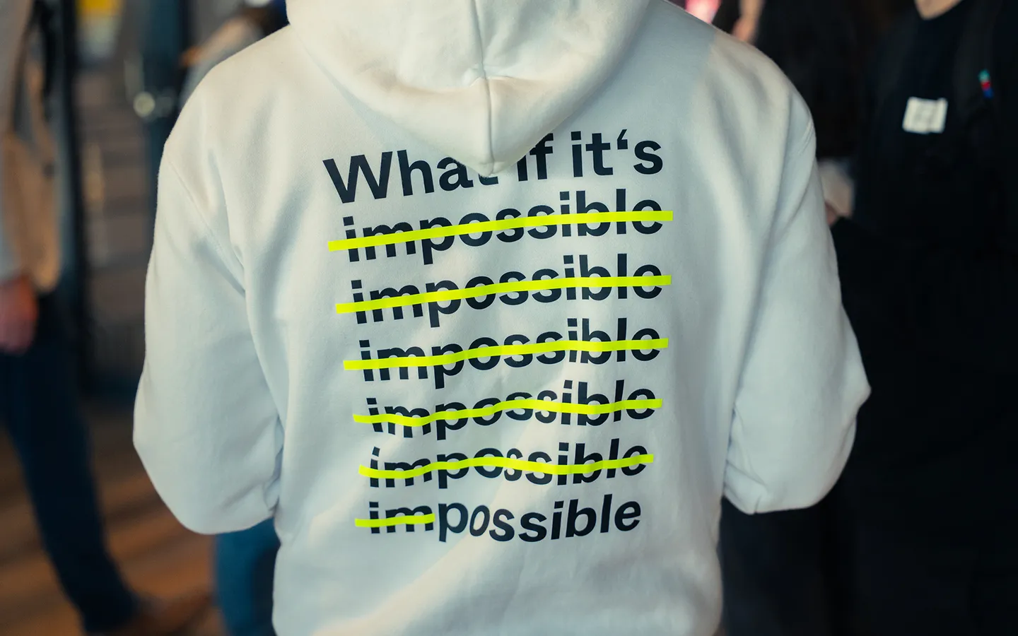 Back of a white hoodie with the phrase 'What if it's impossible' printed multiple times, each 'impossible' crossed out except the last one changing to 'possible'.