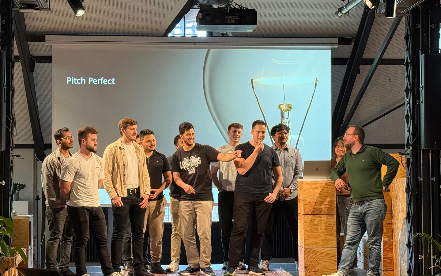 A group of people standing on a stage with a presentation slide behind them that reads 'Pitch Perfect' and shows a lightbulb graphic.