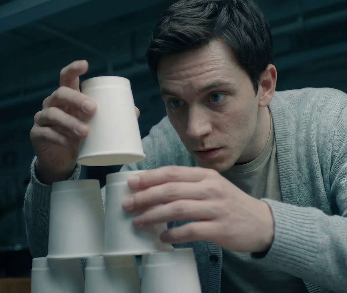 A man carefully stacking white disposable cups into a pyramid shape.