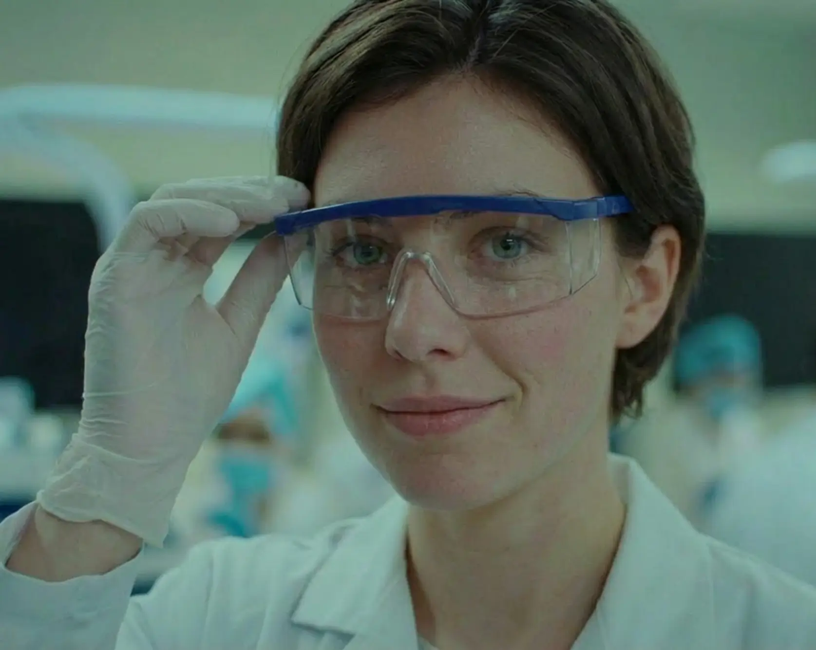 Female scientist wearing protective goggles and gloves, adjusting her eyewear in a laboratory setting.
