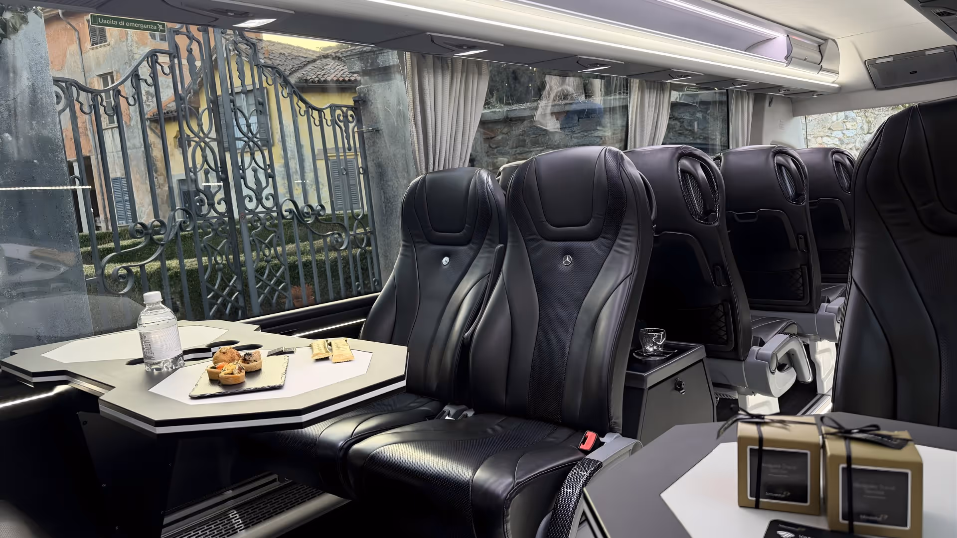 Interior of a Moveolux luxury minibus with black leather seats, snack platter and refreshments on board.