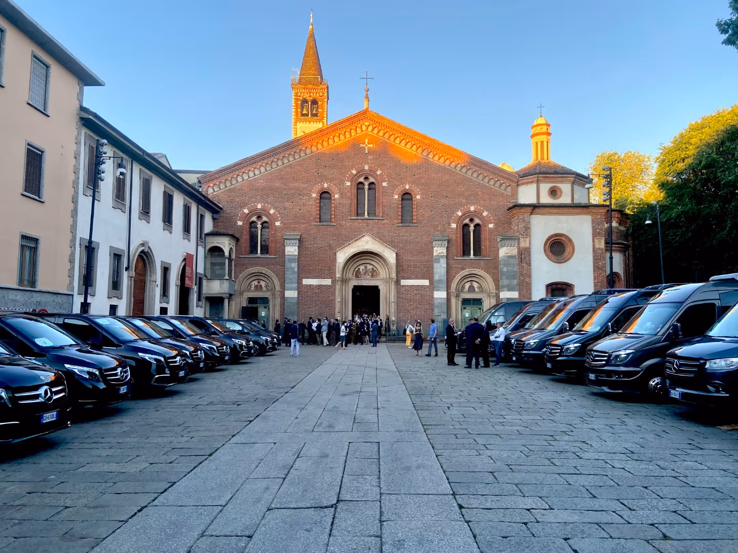 Black Mercedes vans lined up outside a large brick church with people gathered at the entrance.