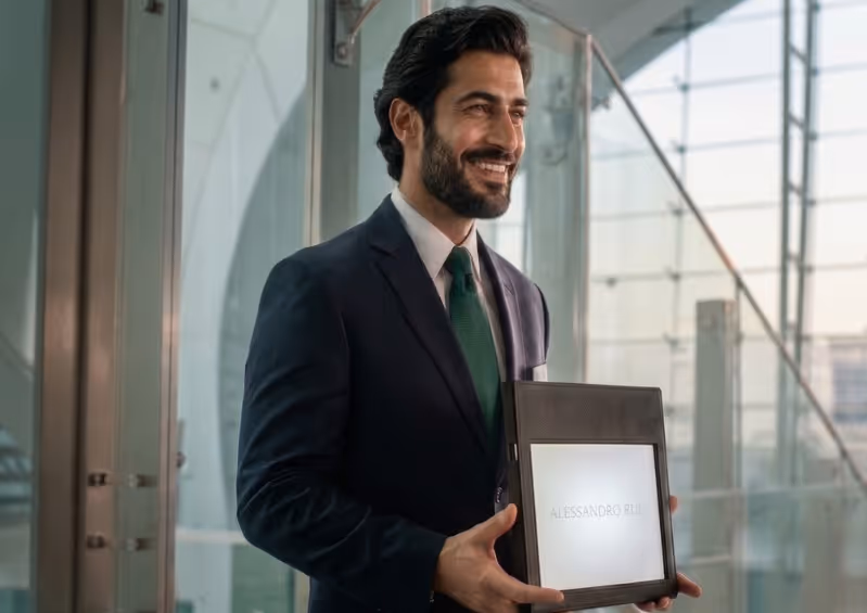 Smiling greeter from Moveolux meet and greet service in a suit holding a welcome sign at an airport arrival area.