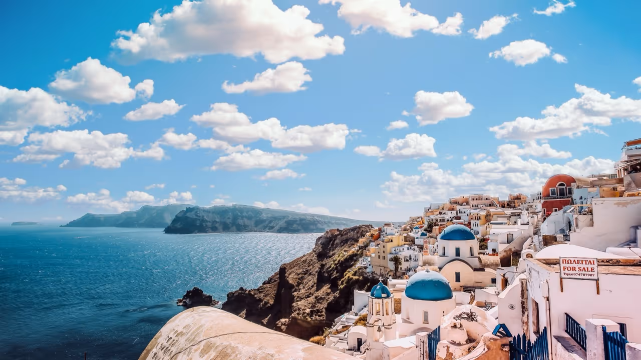 Coastline with white buildings and blue domes under in Greece, a destination for Moveolux yacht charter.