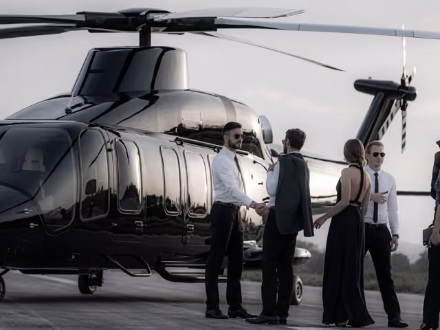 Elegant people dressed in formal wear boarding a sleek black helicopter on a tarmac.