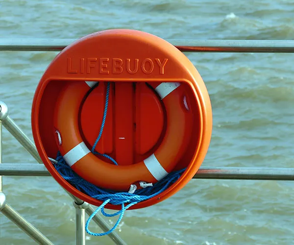 Orange lifebuoy with white stripes in a holder on a metal railing by the water.