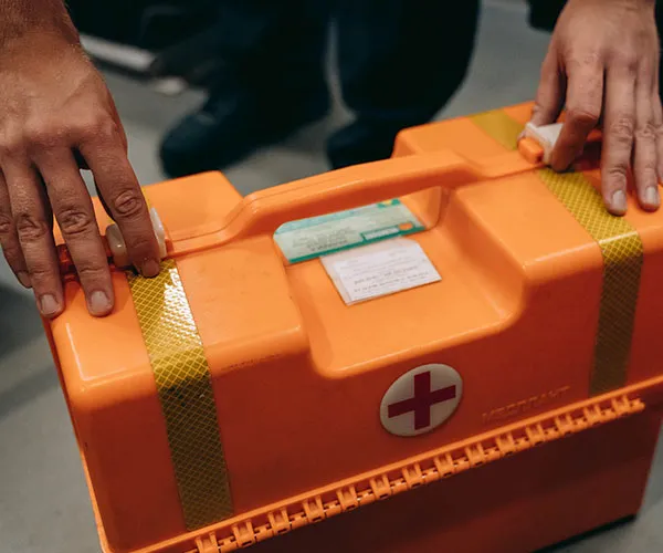 Hands securing the latches of an orange first aid kit box with a red cross symbol.
